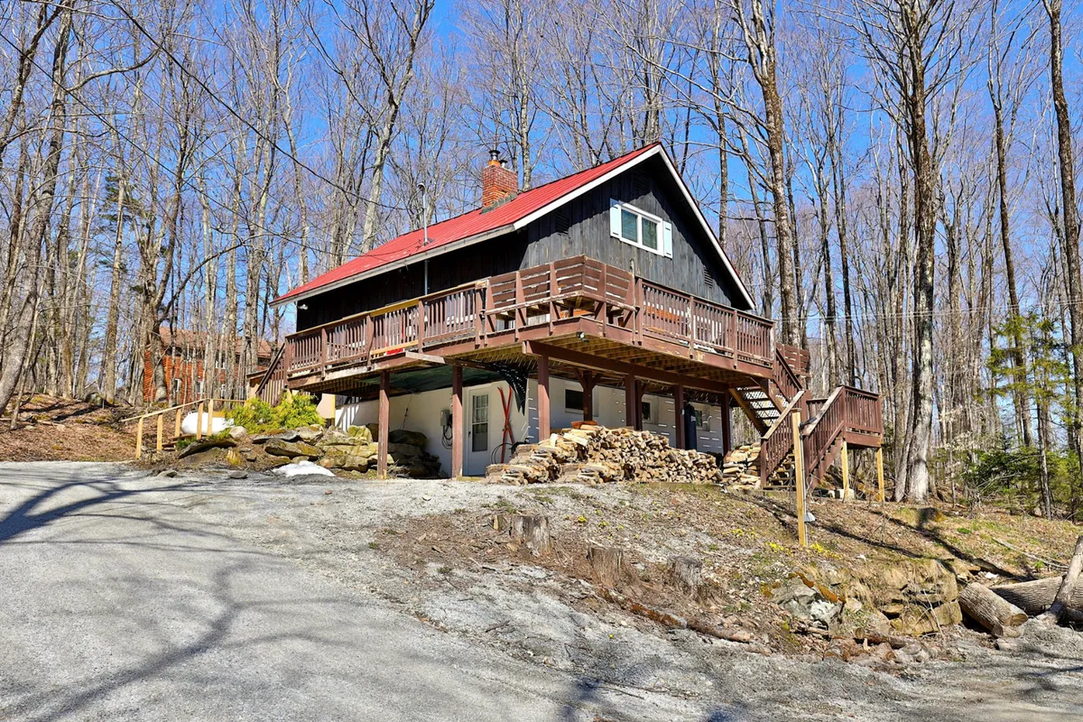 This image highlights a rustic wooden deck with a red roof and surrounding trees, suggesting a cozy, inviting space for outdoor gatherings. A stack of firewood hints at warmth and comfort, while the spacious deck is perfect for barbecues and alfresco dining.