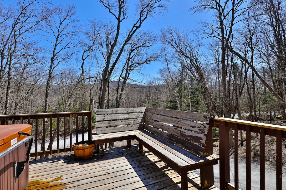 This image showcases a private outdoor deck area featuring a hot tub set amid surrounding trees, with wooden seating available for guests. The atmosphere is tranquil and the view suggests a perfect space for relaxation or gathering with friends and family, especially after a day on the slopes.