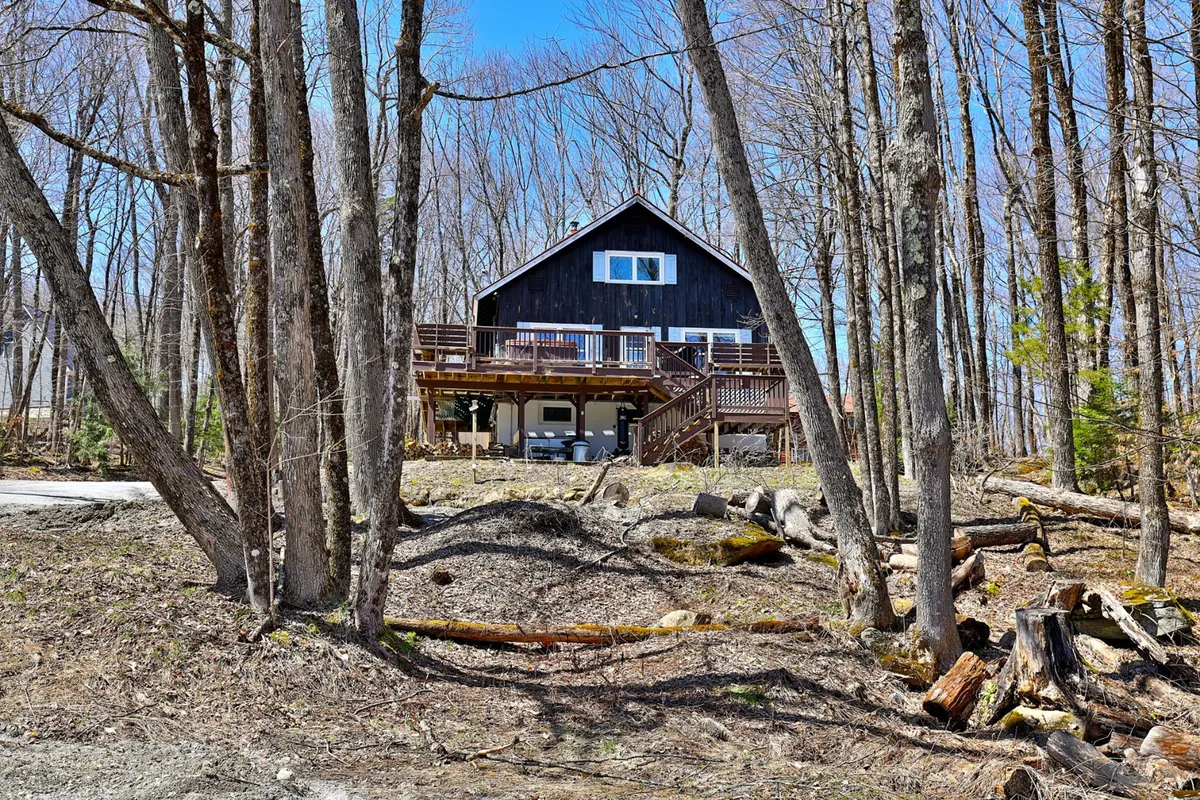 This exterior shot highlights the house, its spacious deck, and the surrounding trees. The view suggests a peaceful and scenic setting, ideal for relaxing after outdoor activities or gearing up for adventure. The deck is prominently featured, hinting at opportunities for après-ski BBQs and social gatherings.