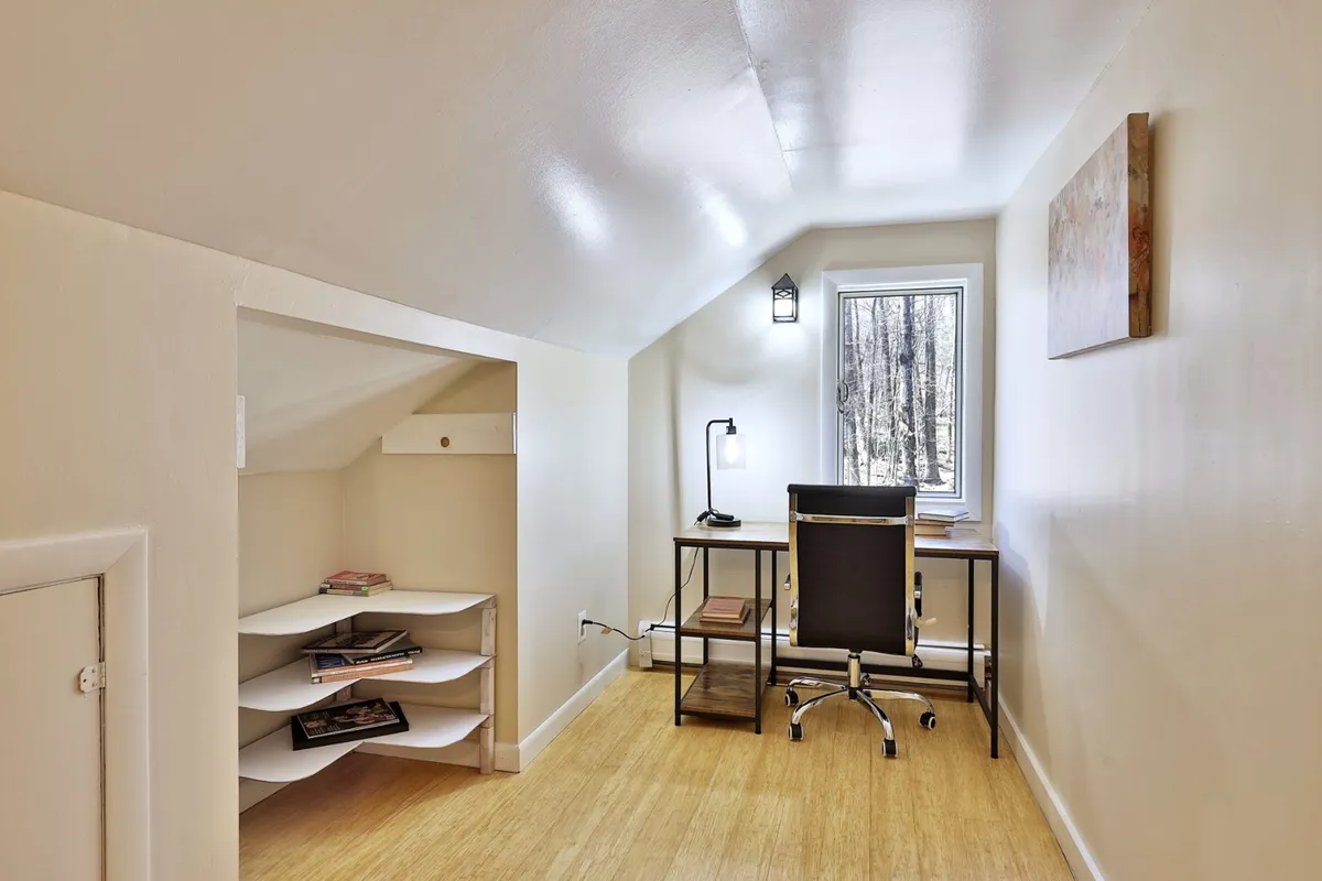 A bright office nook featuring a desk with a lamp, shelves for organization, and a window that lets in natural light, creating a productive yet serene environment. The setup is uncluttered and inviting, ideal for working, reading, or planning activities.