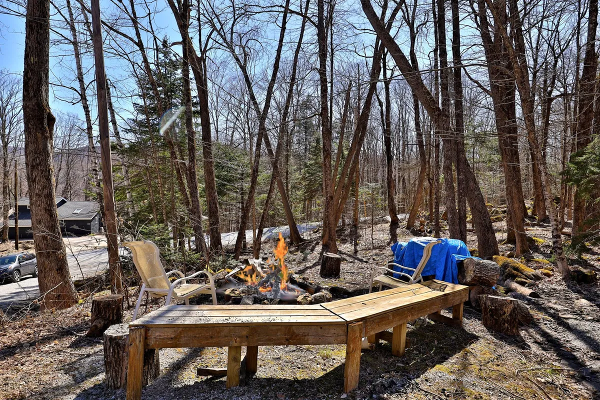 An inviting outdoor fire pit area surrounded by wooden seating and nestled among the trees. The scene suggests warmth and camaraderie, perfect for post-adventure campfire gatherings or relaxing under the stars after an active day in the snow.