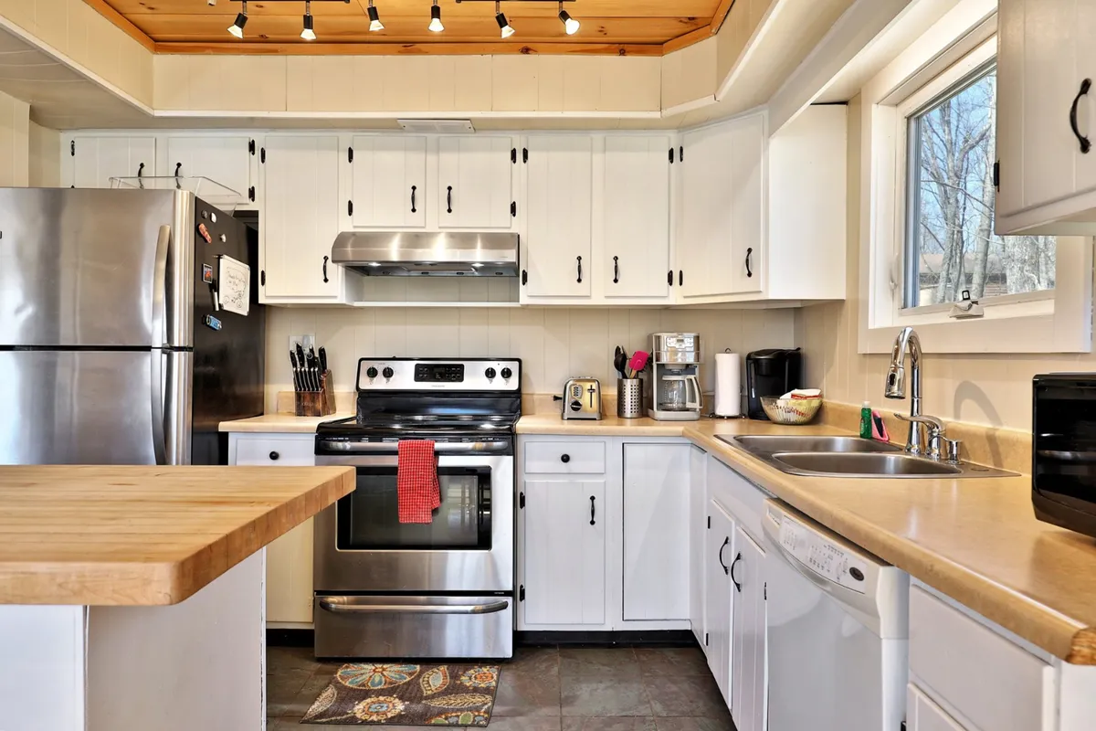 A modern kitchen with stainless steel appliances, a sleek wooden countertop, and a sink positioned below a window offering an outdoor view. The space feels functional yet homey, ideal for preparing meals, baking with children, or hosting group dinners.