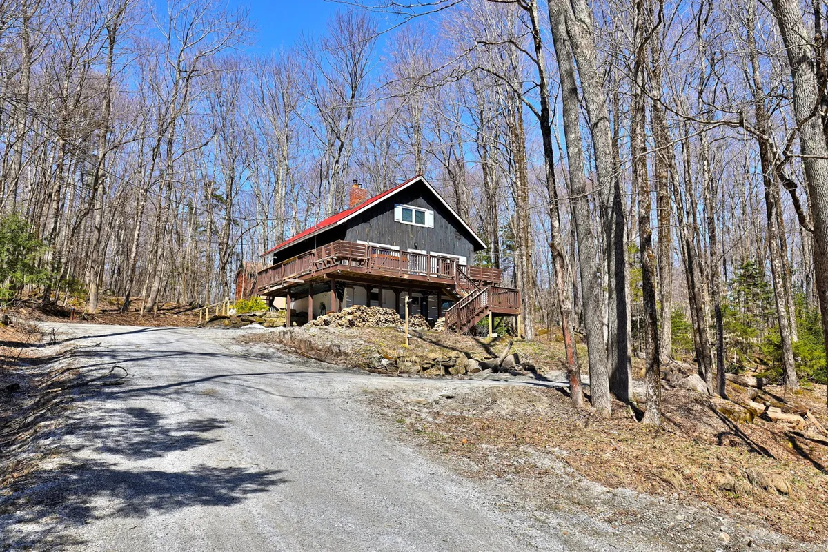The exterior of the house, showcasing the front entrance with a wooden deck and gravel driveway, surrounded by nature. The scene hints at privacy, secure entry, and a peaceful mountain atmosphere.