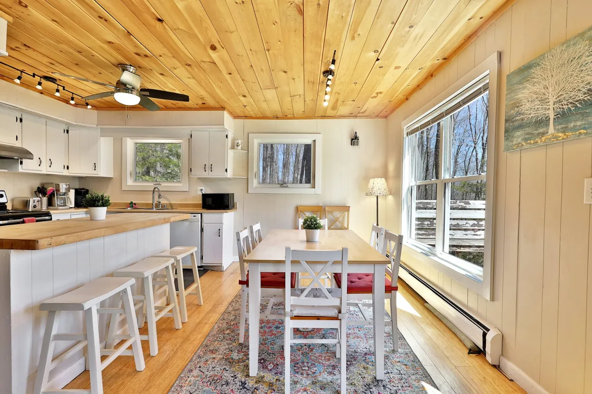 A cozy dining area with a large table is set near the kitchen island and a generous window that bathes the space in natural light. The scene is perfect for family meals, casual gatherings, and celebrations, with artwork adding a touch of personality.
